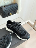 Chanel women’s lace-up sneakers in dark black, angled side view on a gray box.