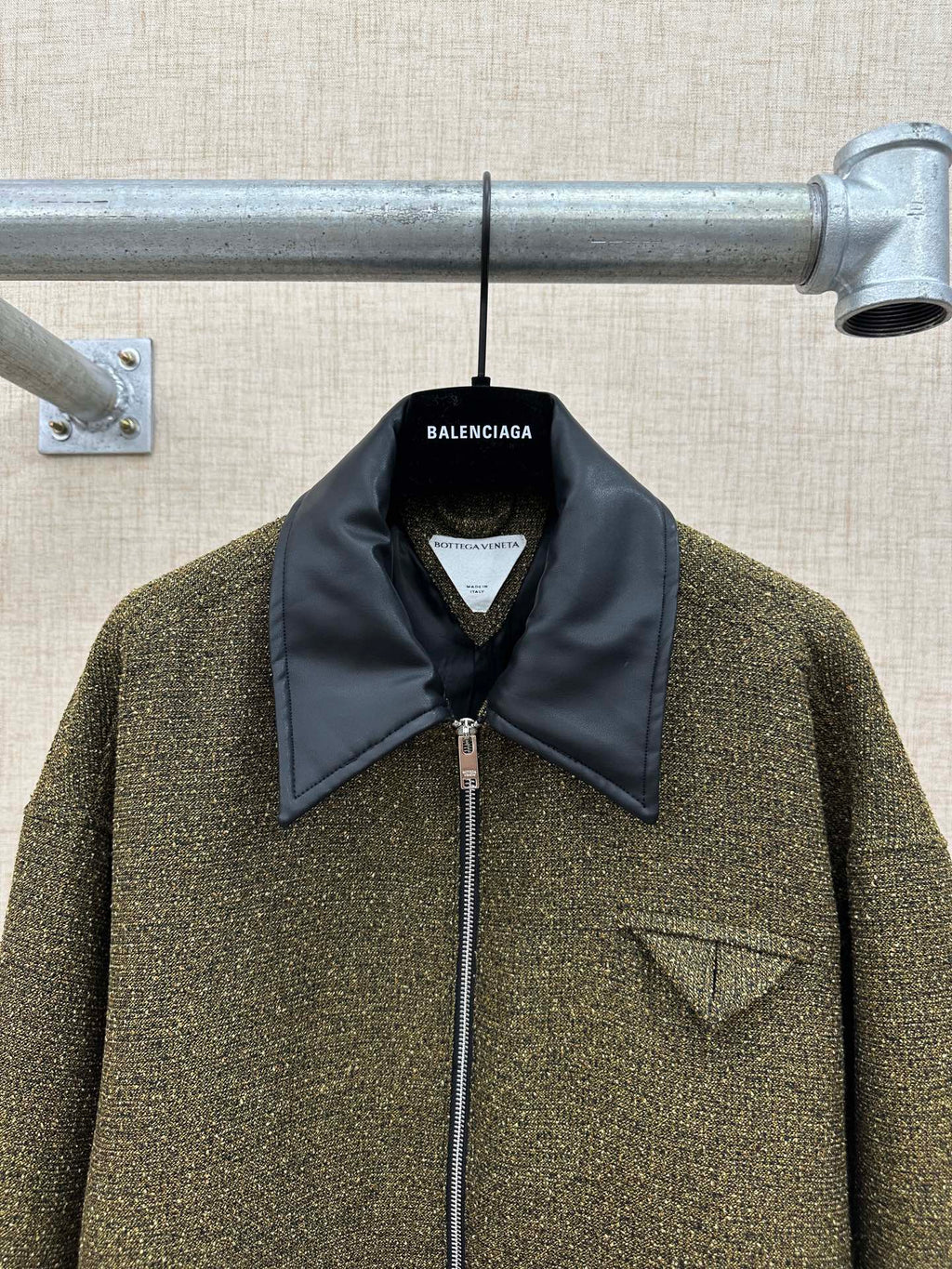 Olive textured jacket front with dark blue collar, zipper, and small triangle chest patch