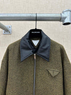 Olive textured jacket front with dark blue collar, zipper, and small triangle chest patch