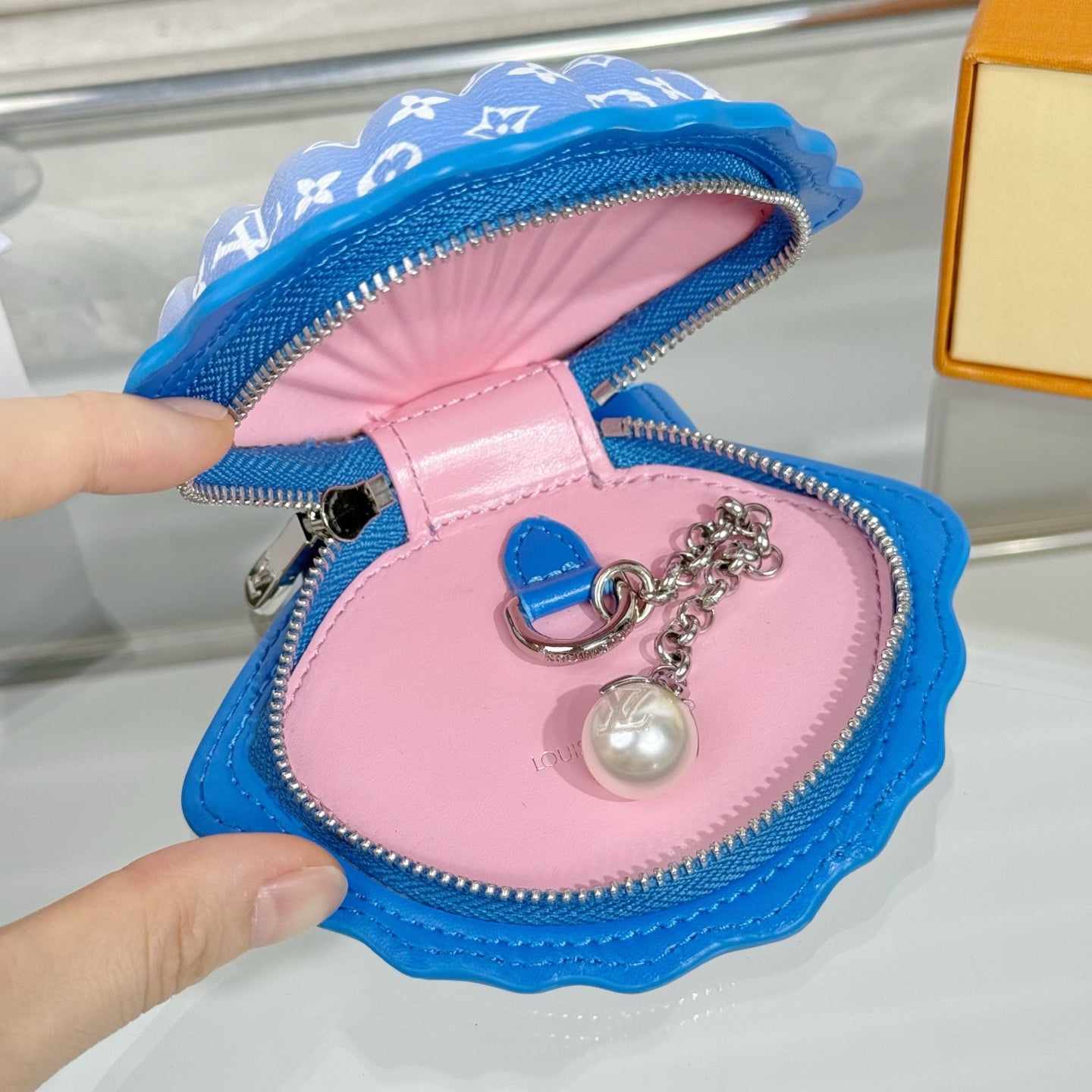 Small monogram pouch bag with blue exterior, pink lining, and pearl charm on chain