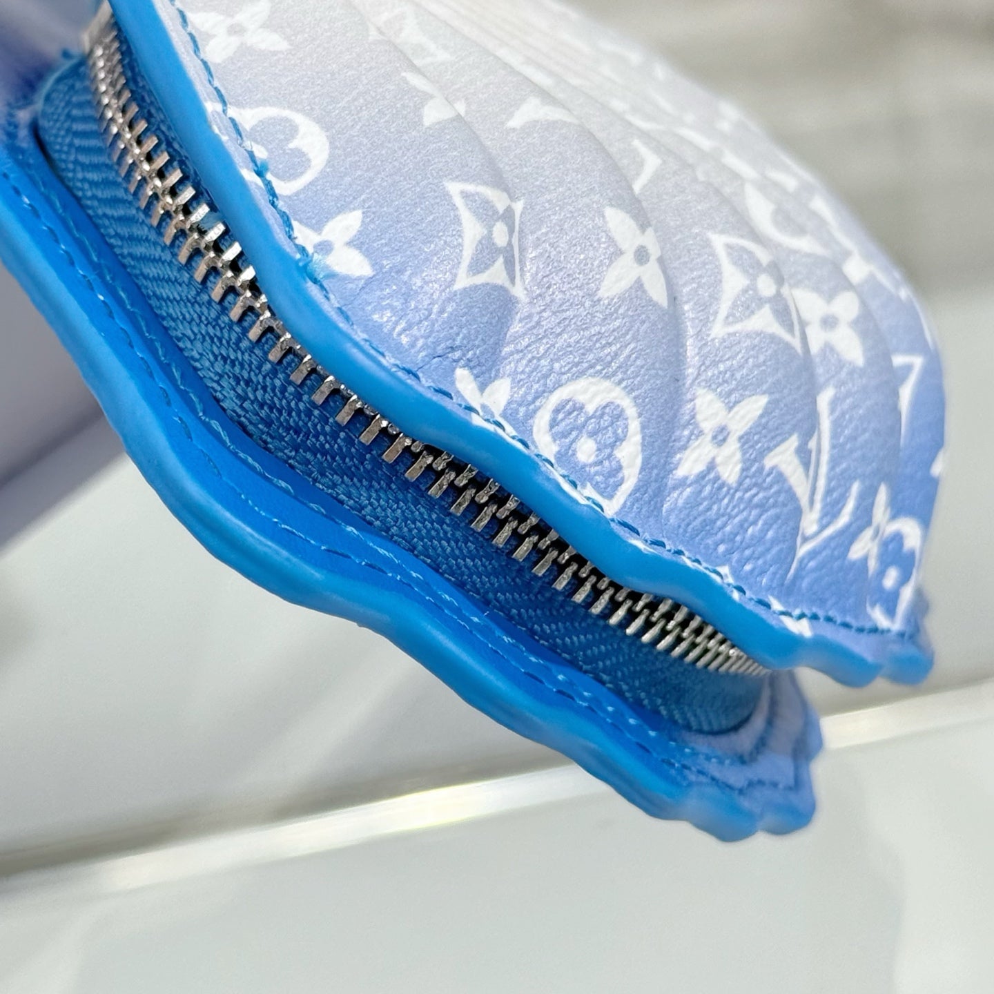 Small monogram pouch bag side view with zipper track and blue textured trim