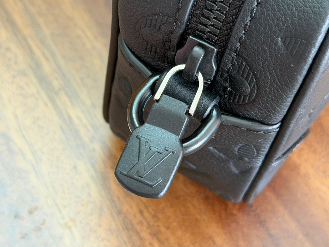 Louis Vuitton monogram bag with metal clasp and strap hardware on dark leather.