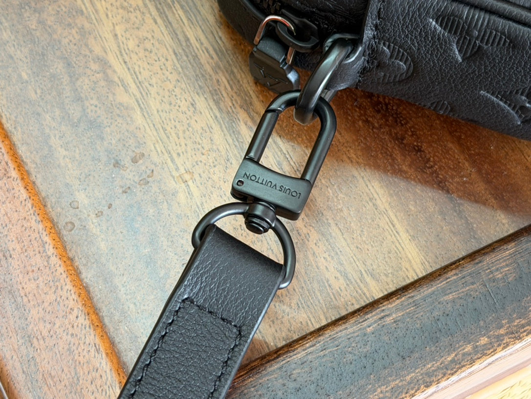 Louis Vuitton crossbody strap with keyring clasp and engraved hardware attachment.