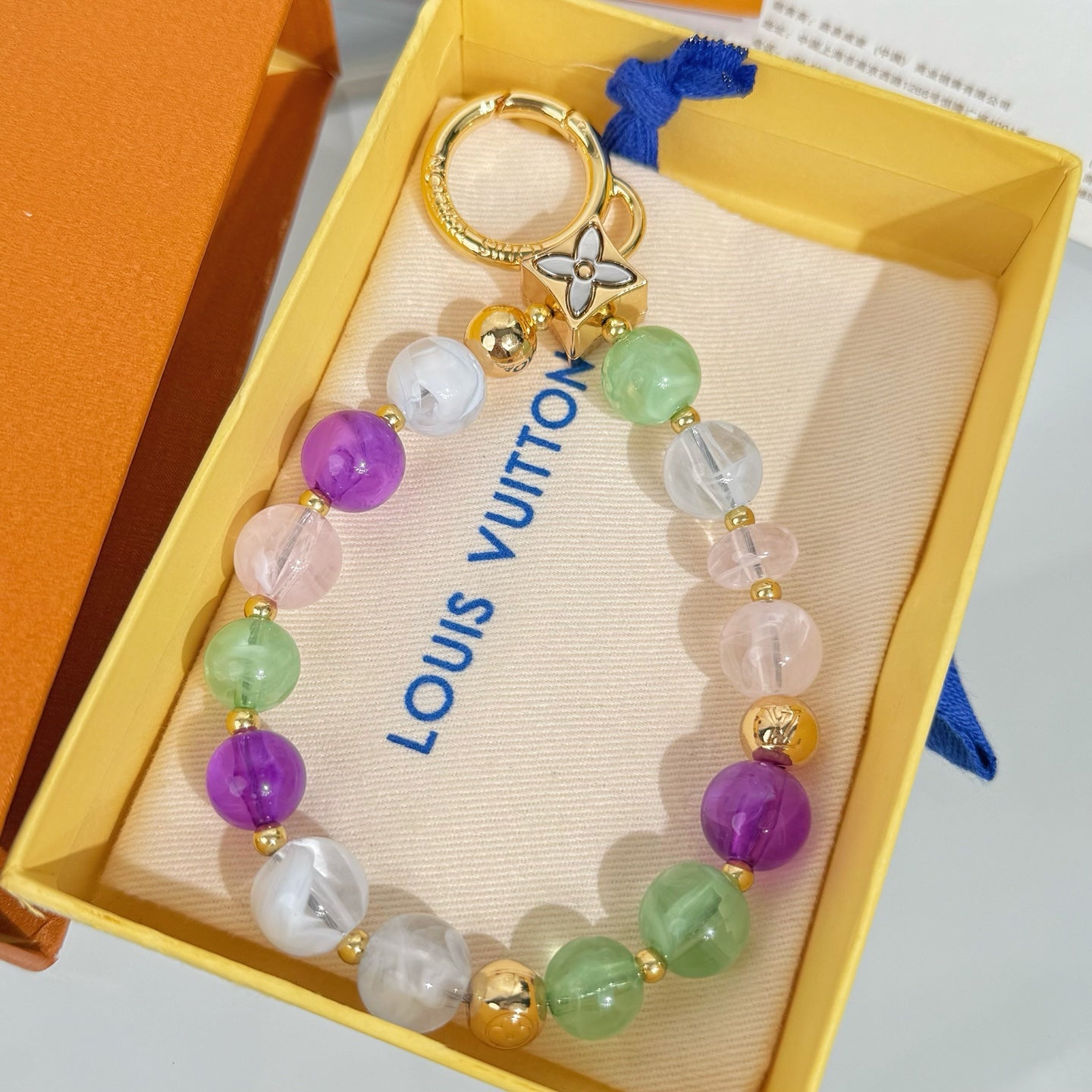 Beaded charm bracelet with gold key ring, multicolor beads, and blue tassel in box