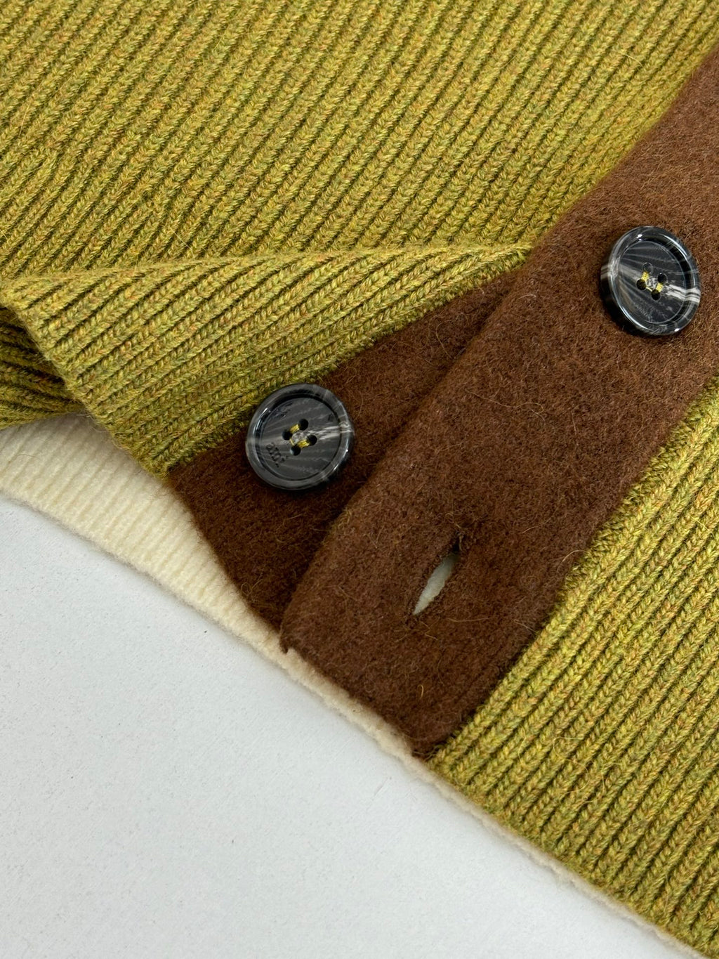 Green knit cardigan hem detail with brown buttons and cream cuff trim