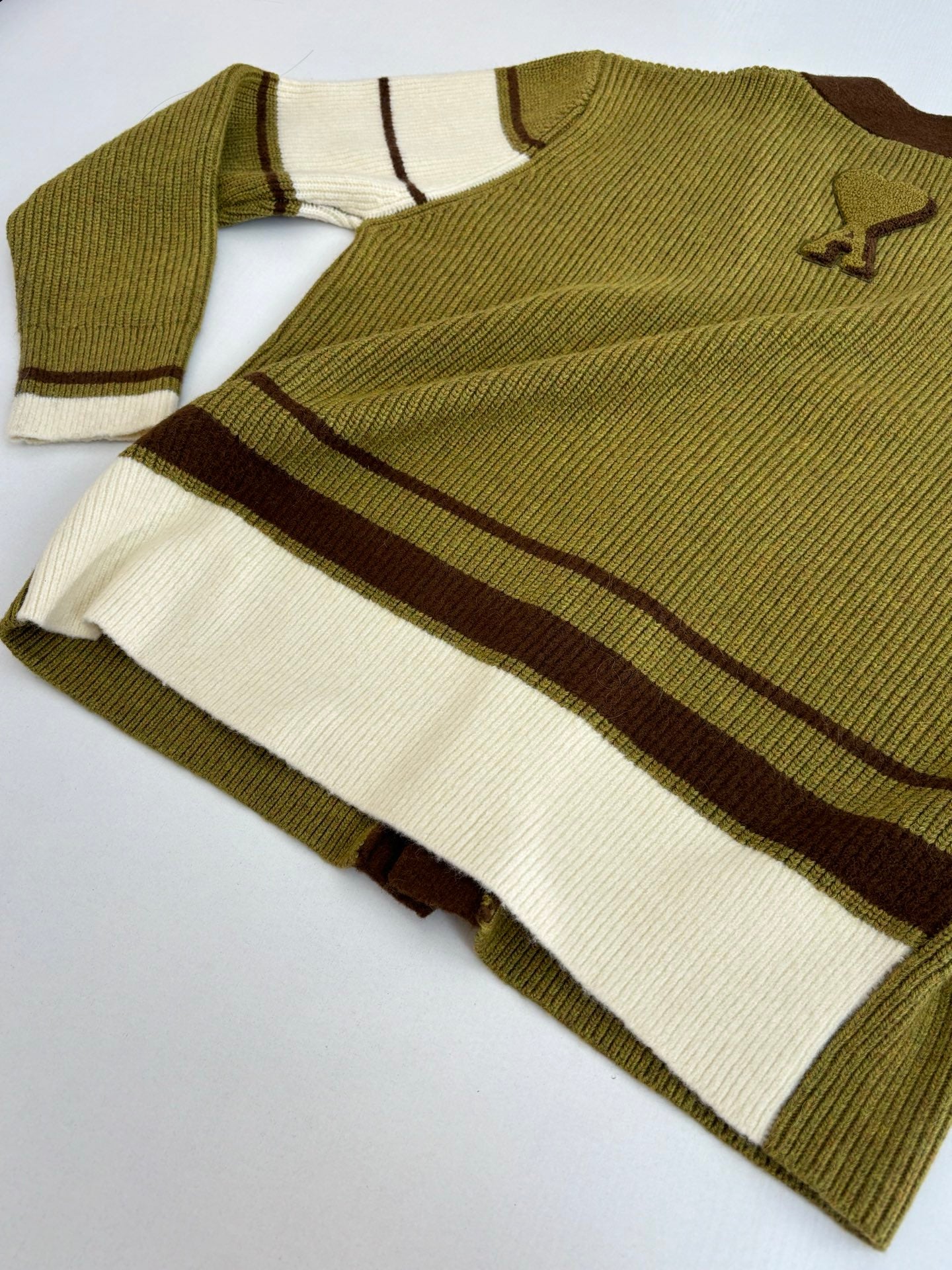 Folded knit sweater with olive body, white and brown stripes, and logo on sleeve