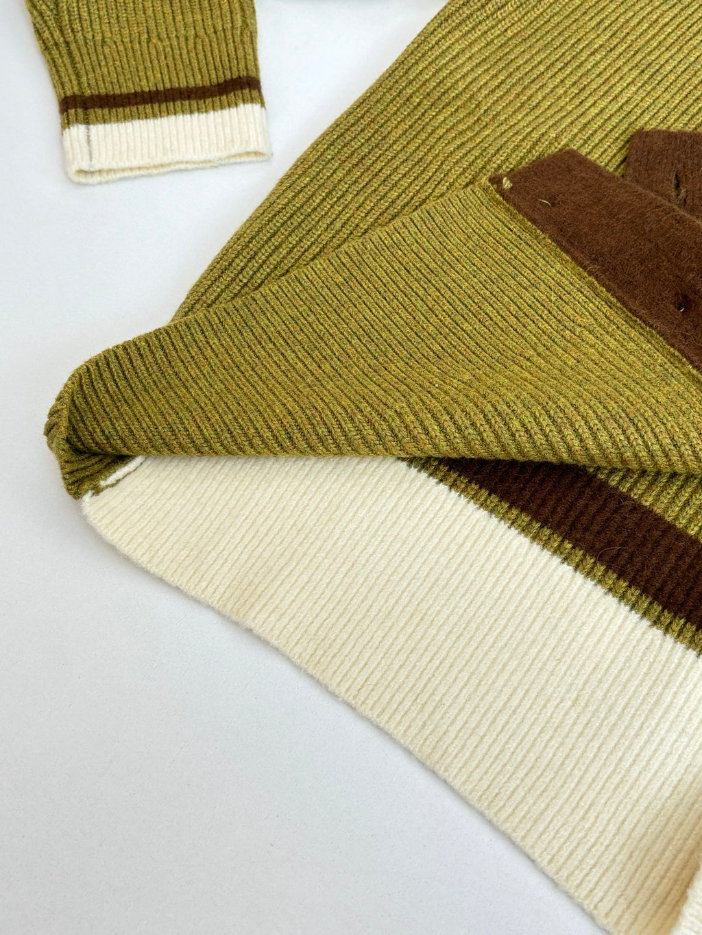 Green knit cardigan hem with cream ribbed trim and brown underlay
