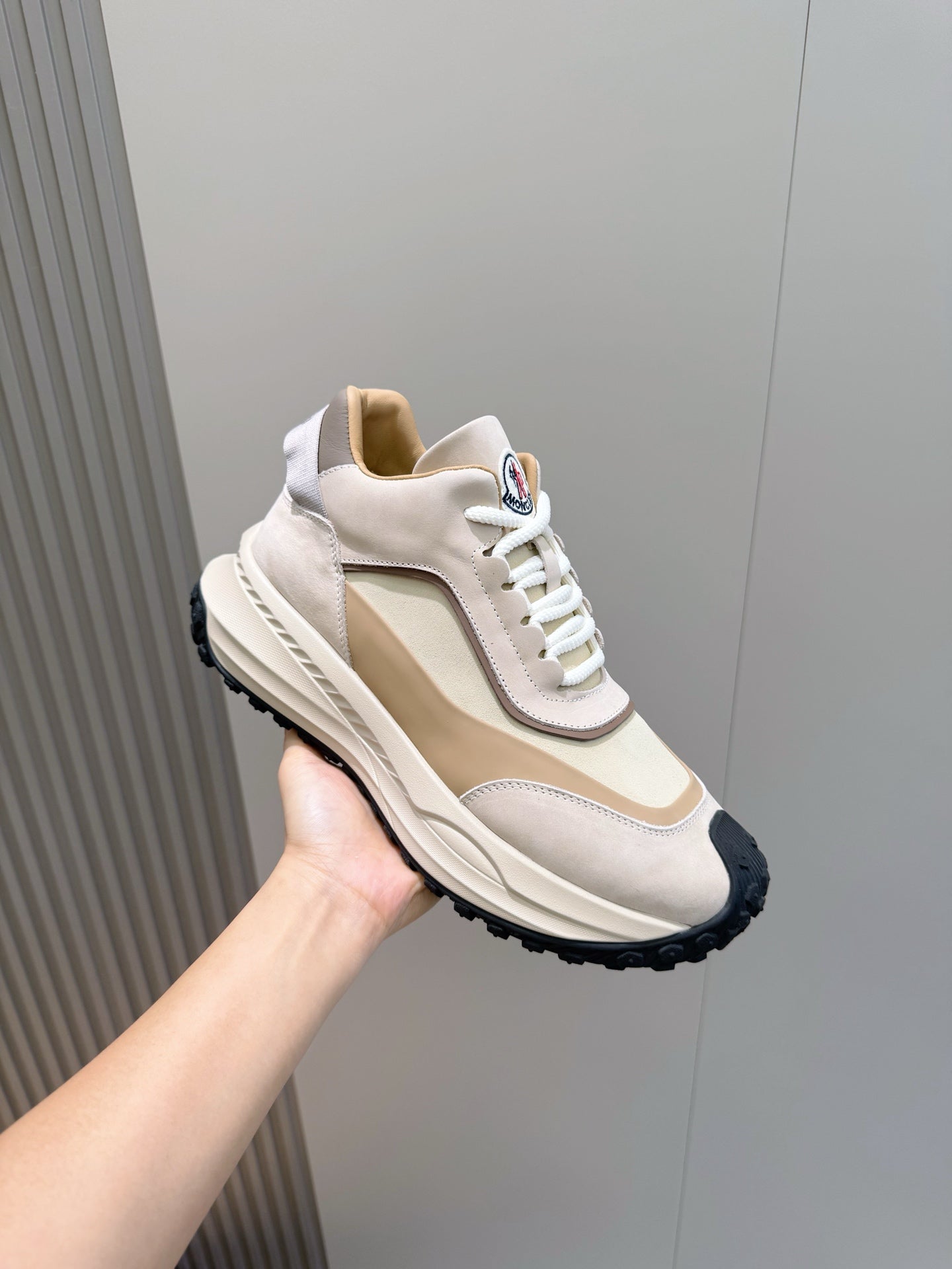 Moncler sneaker held in hand, beige and off-white with white laces and dark outsole