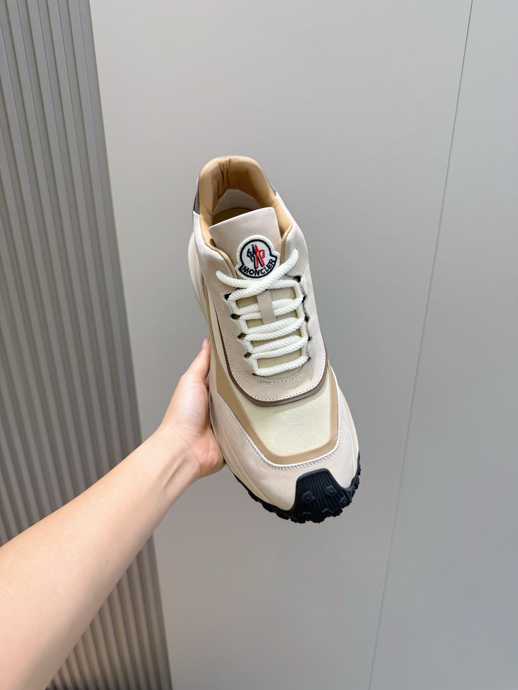 Moncler sneaker held in hand, beige and cream upper with white laces