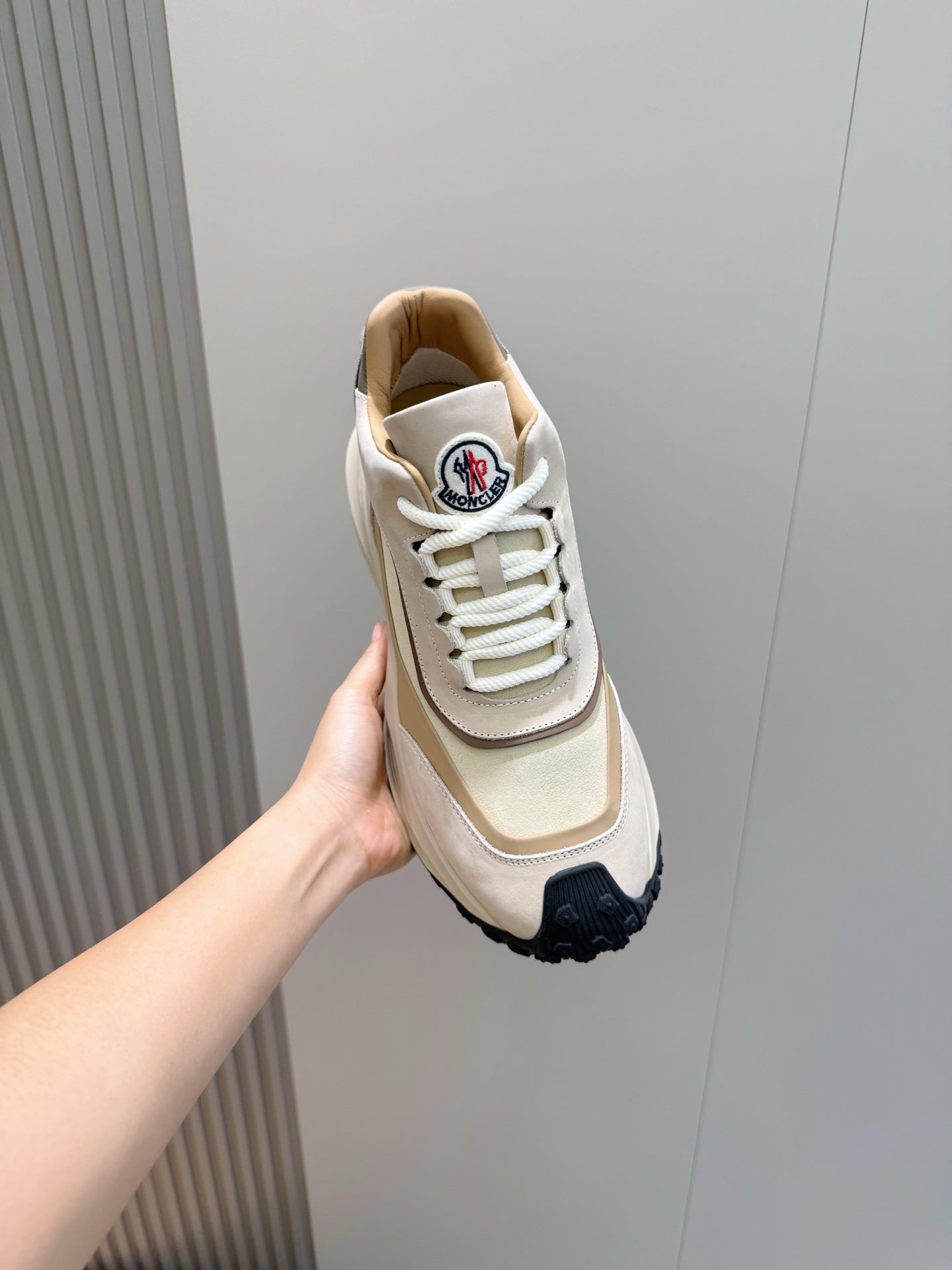 Moncler sneaker held in hand, beige and cream upper with white laces