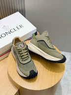 Moncler sneakers on display, sage green upper with navy heel trim and white sole