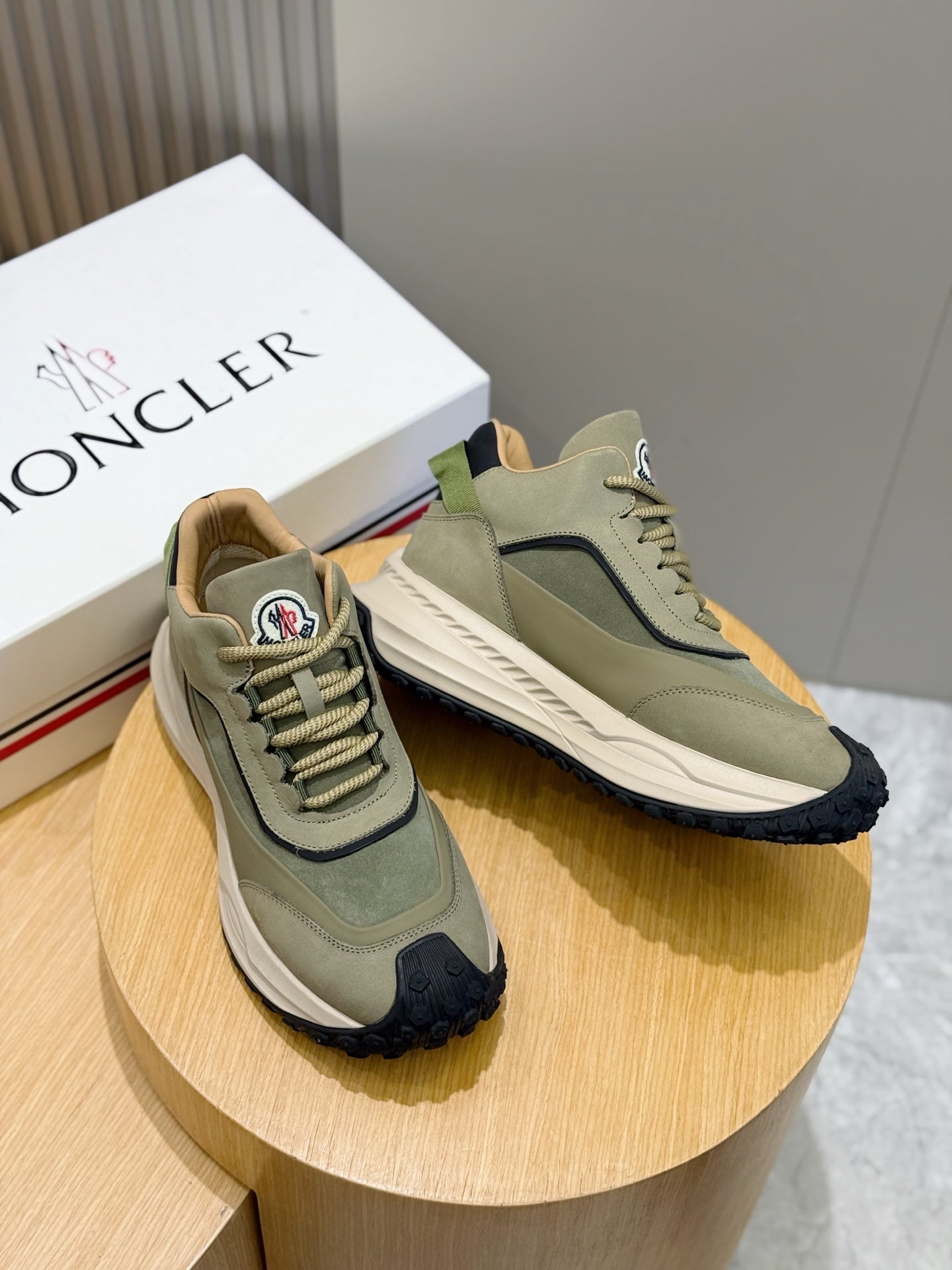 Moncler sneakers on display, sage green upper with navy heel trim and white sole
