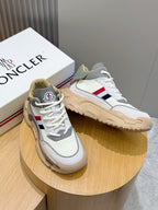 White Moncler sneakers with tan sole, blue red side stripe, on display stand