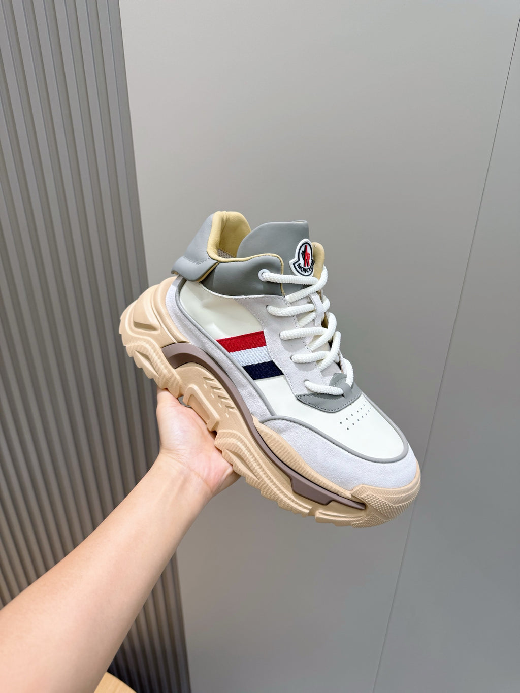Moncler sneaker held at angle, white and light blue with red/blue stripe and chunky sole