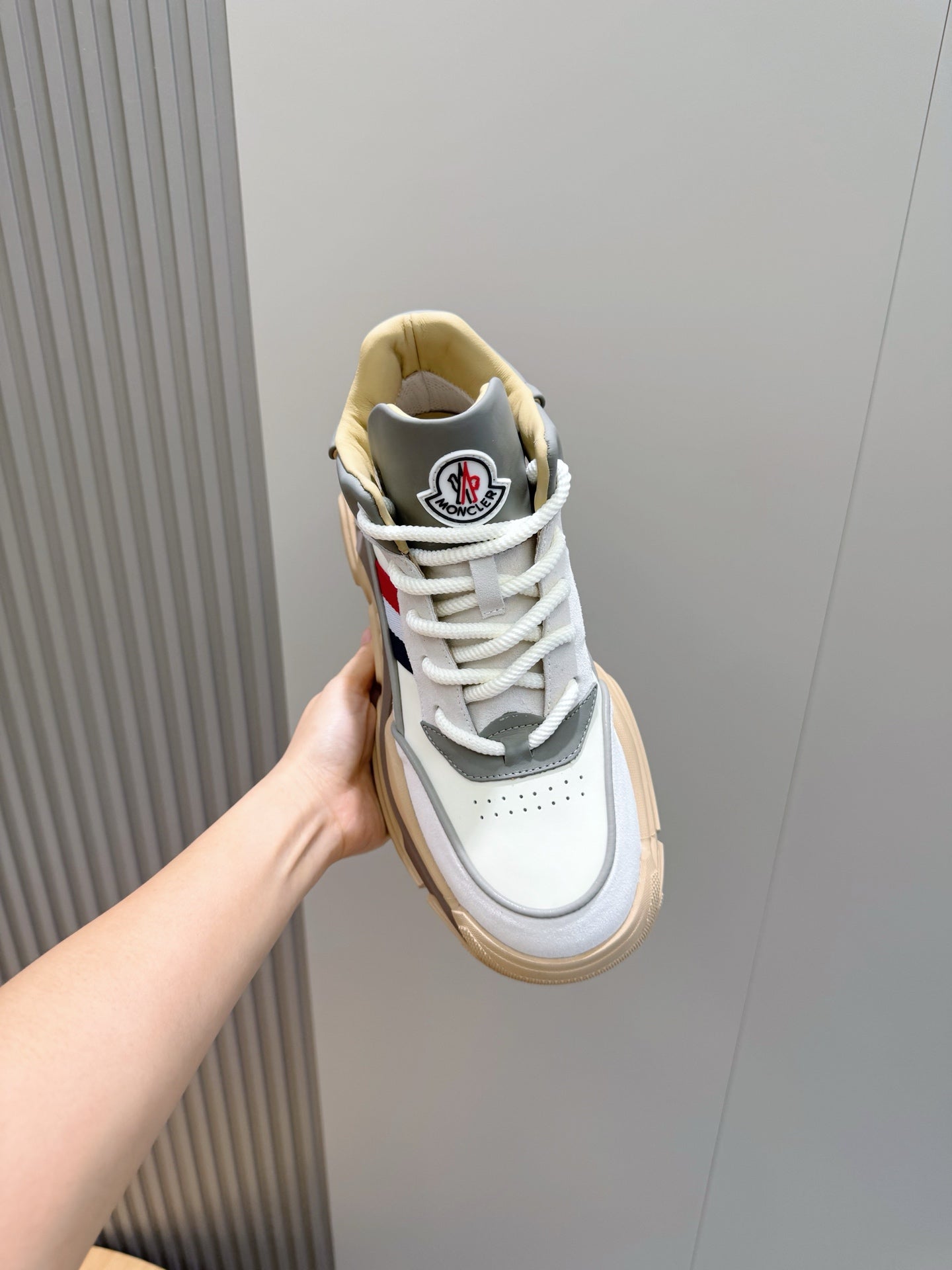 Moncler sneaker held in hand, white upper with dark blue heel patch and beige sole