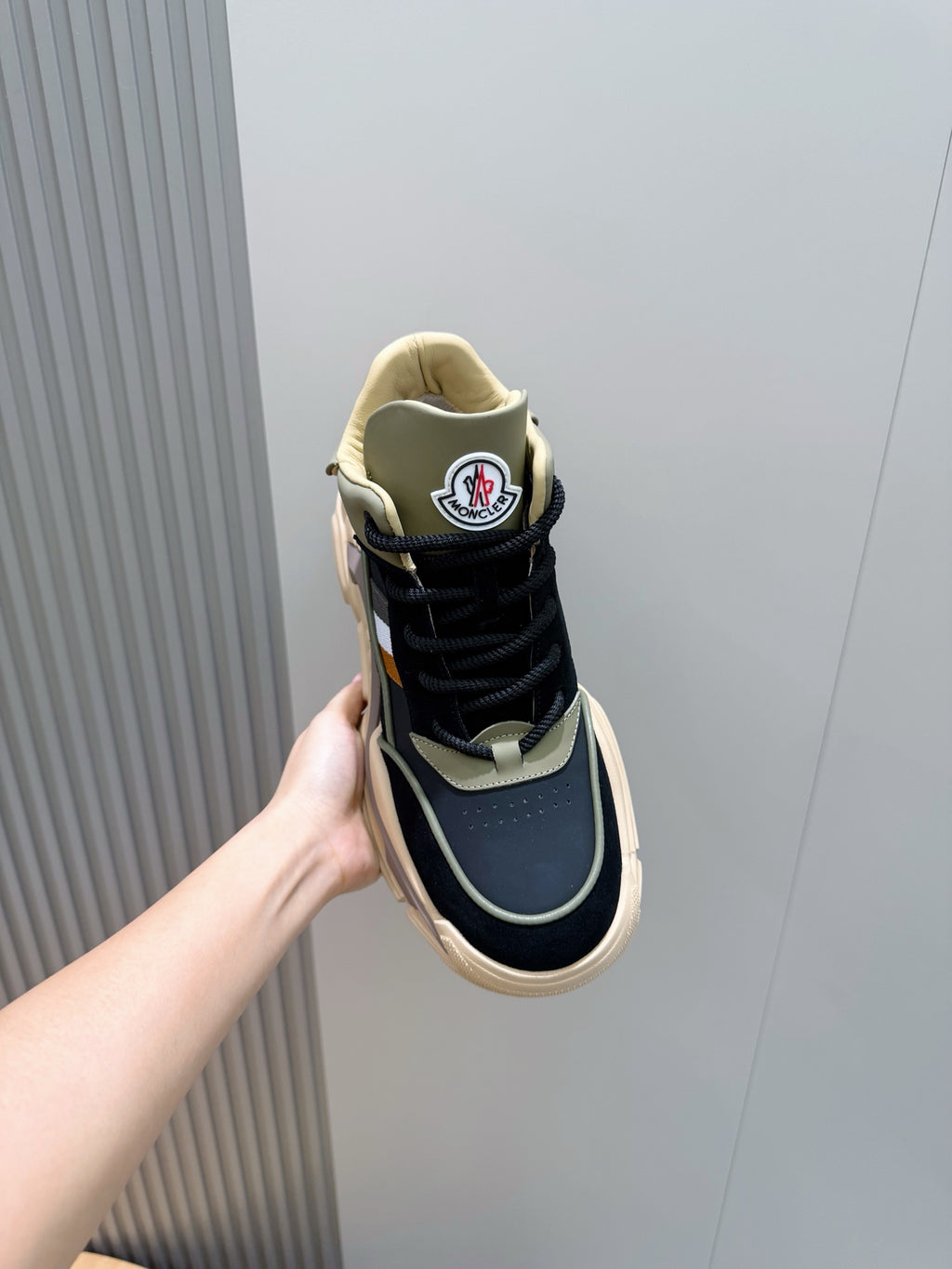Moncler sneaker held by hand, navy upper with beige collar trim and thick sole