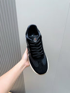 Black lace-up sneakers held up, showing side panel logo and white sole
