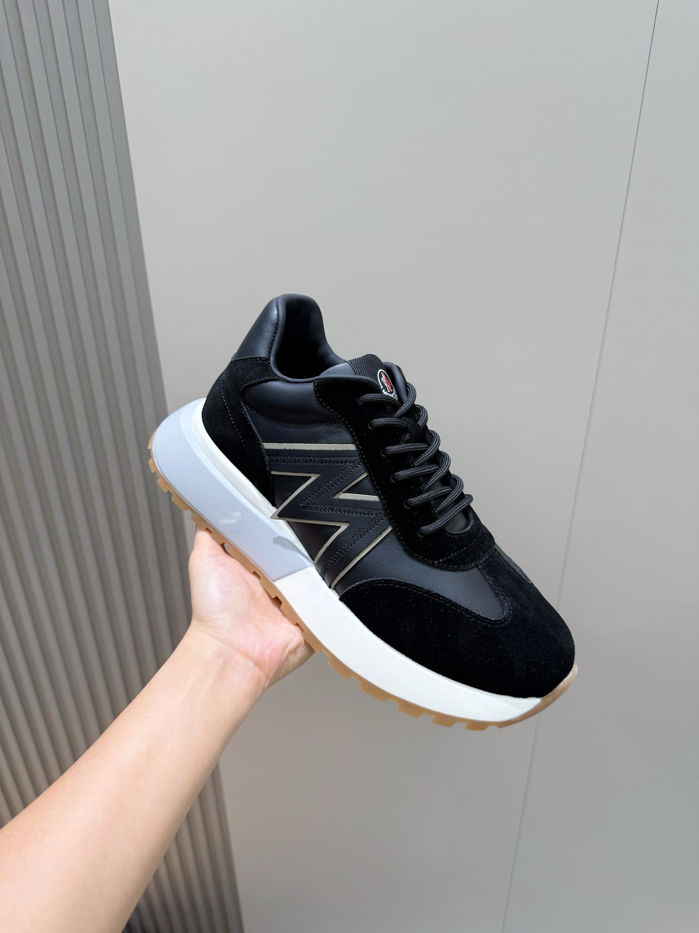 Black sneakers with zigzag side stripe and white midsole, held in hand