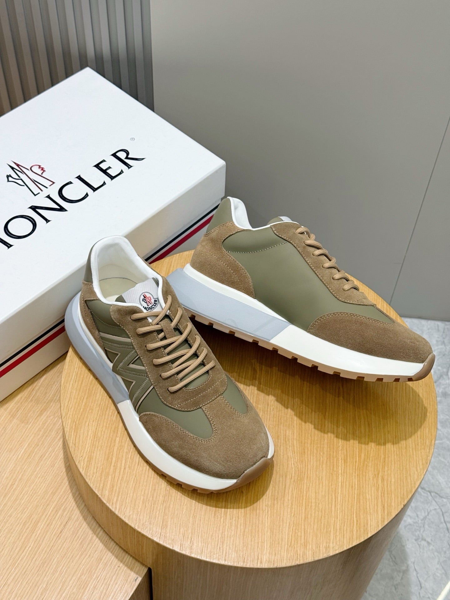Pair of Moncler low-top sneakers in olive and tan suede on a round display
