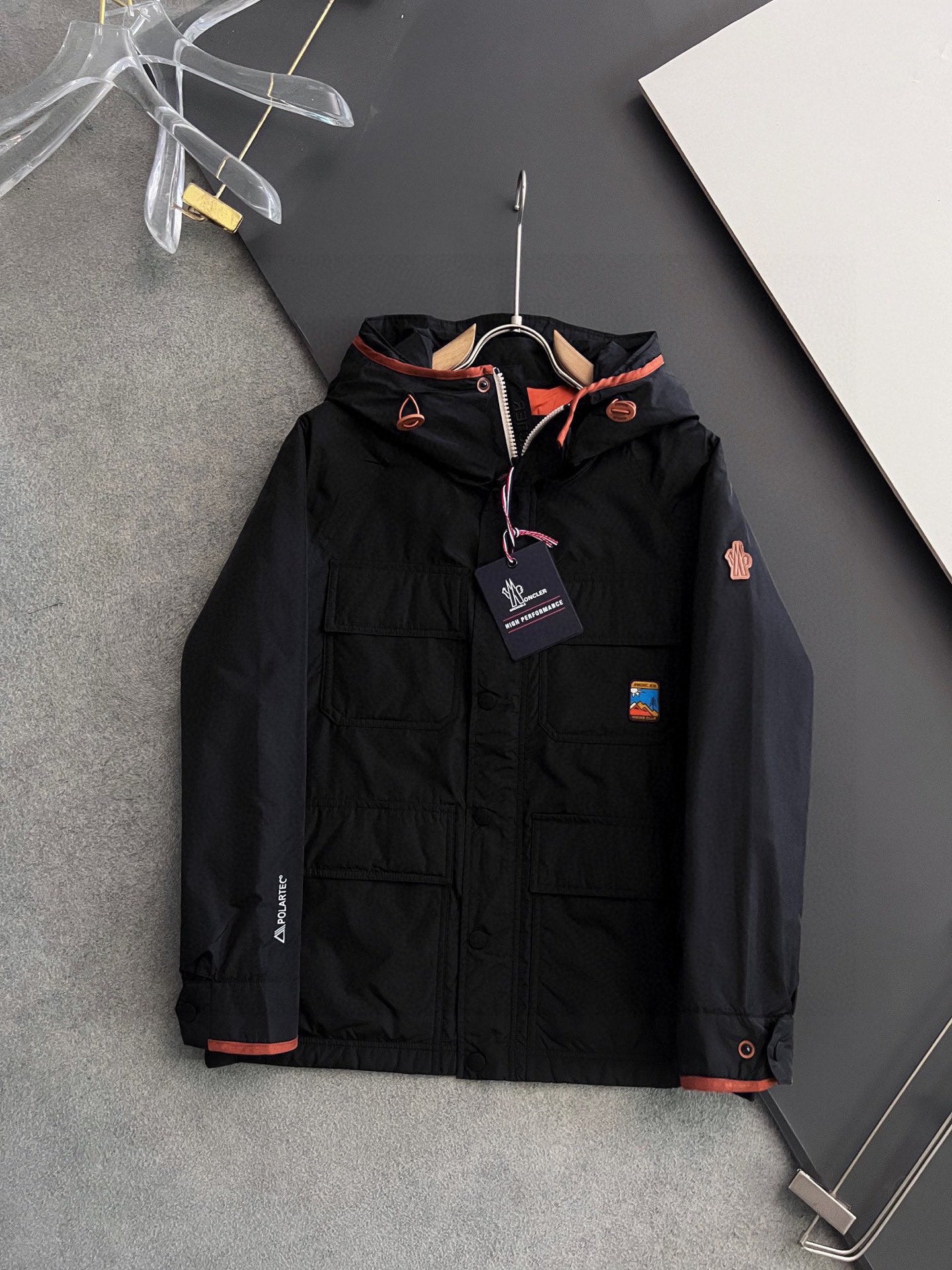 Long black winter jacket with zip front, orange trim, hood and logo patches