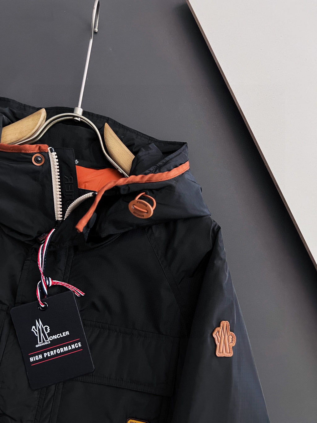 Long black winter jacket detail: hood lining, zip pull, logo patches, orange trim