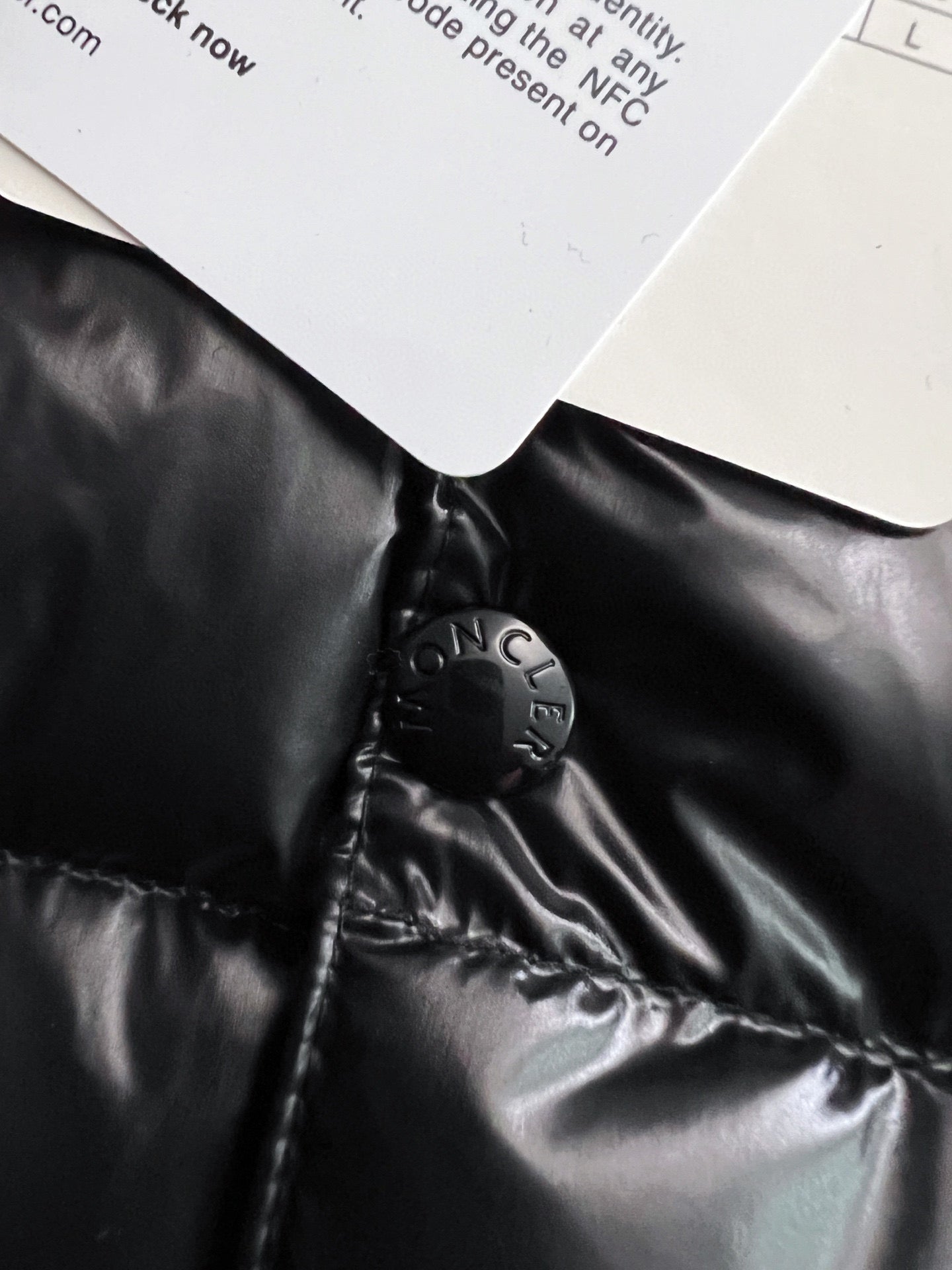 Black puffer jacket collar area with Moncler-engraved snap hardware