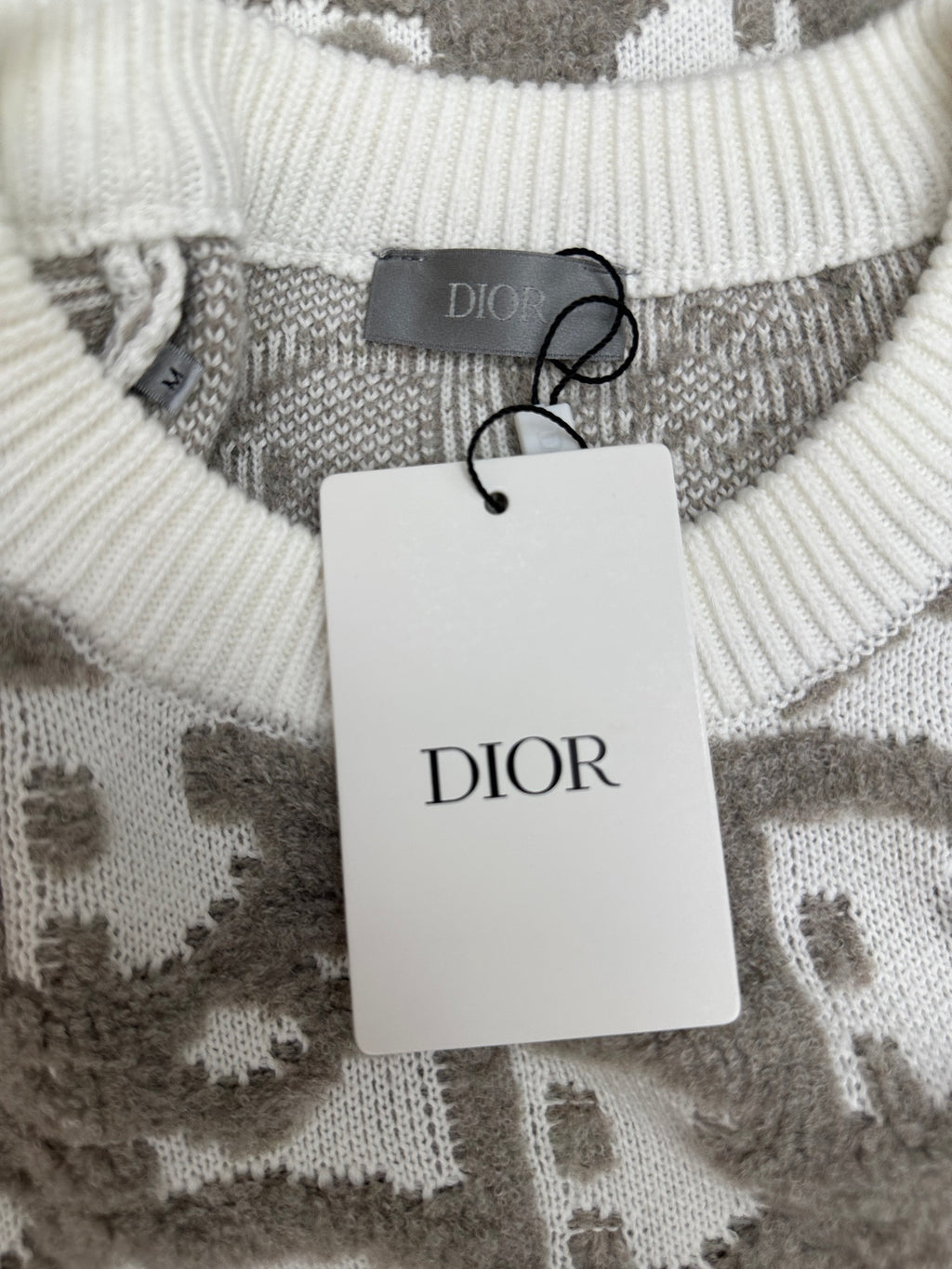 Crew-neck ribbed knit sweater with DIOR tag hanging on gray and white logo-like pattern