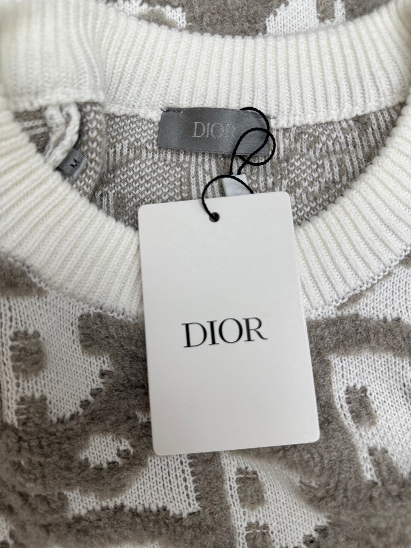 Crew-neck ribbed knit sweater with DIOR tag hanging on gray and white logo-like pattern