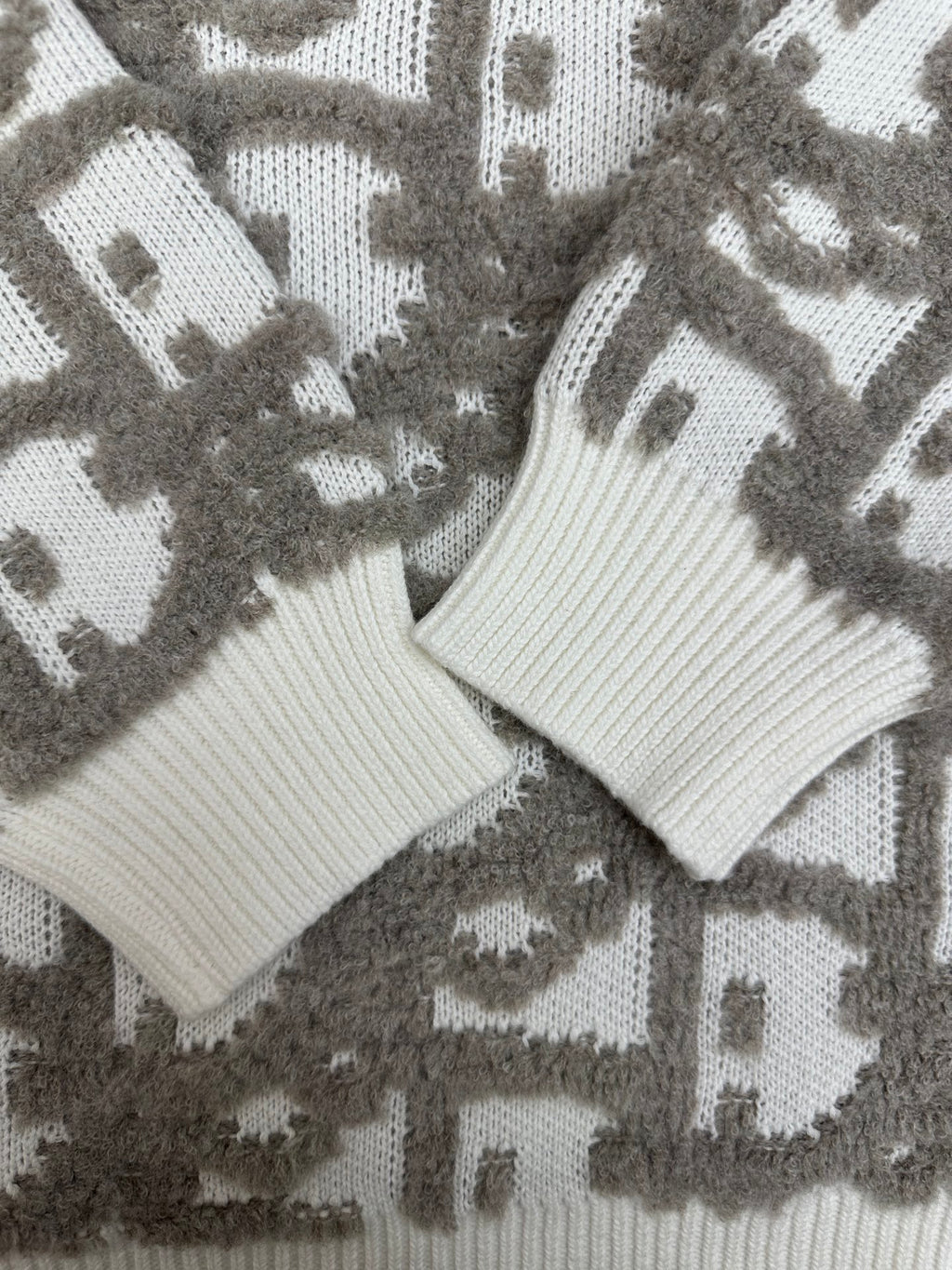 Close-up of knit sweater cuffs and hem in white ribbing on gray logo-like pattern