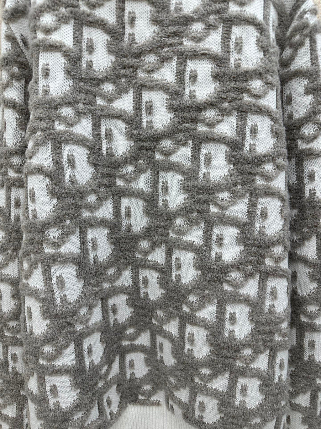 Close-up of gray and white knit sweater with repeating logo-like pattern