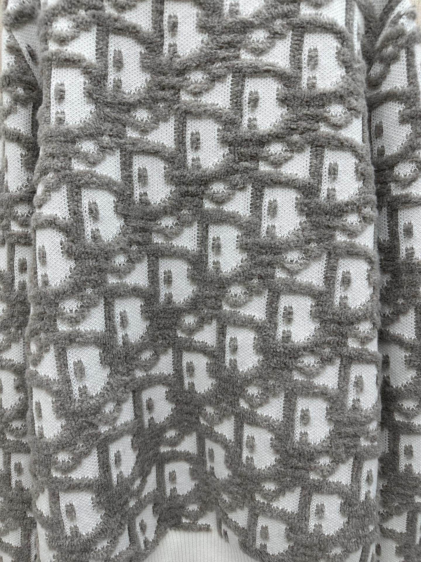 Close-up of gray and white knit sweater with repeating logo-like pattern