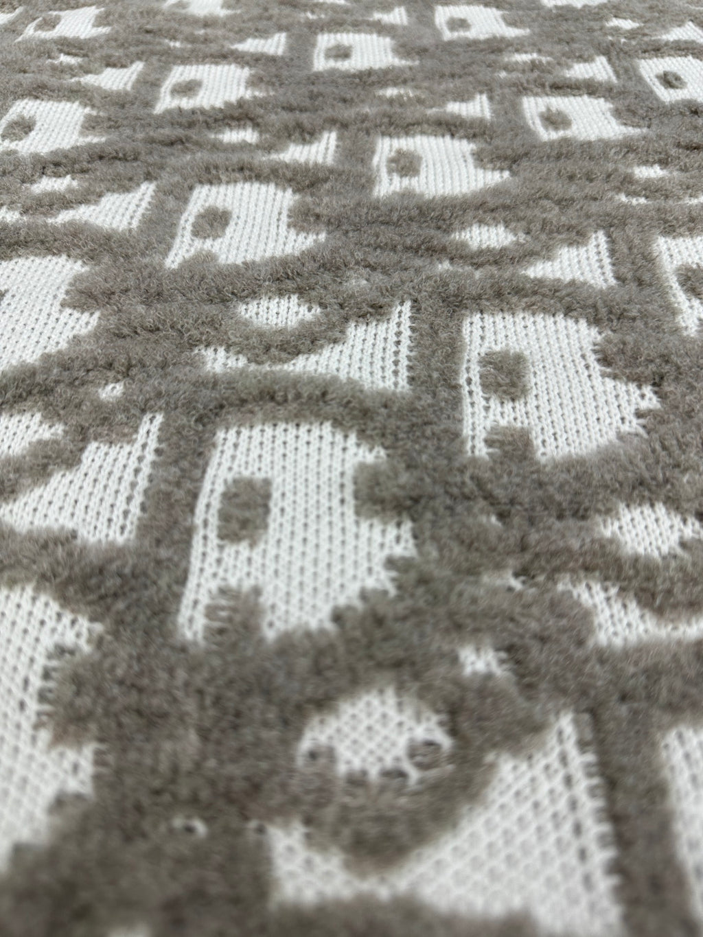 Close-up of knit fabric with repeating gray and white logo-like motifs