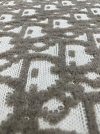 Close-up of knit fabric with repeating gray and white logo-like motifs