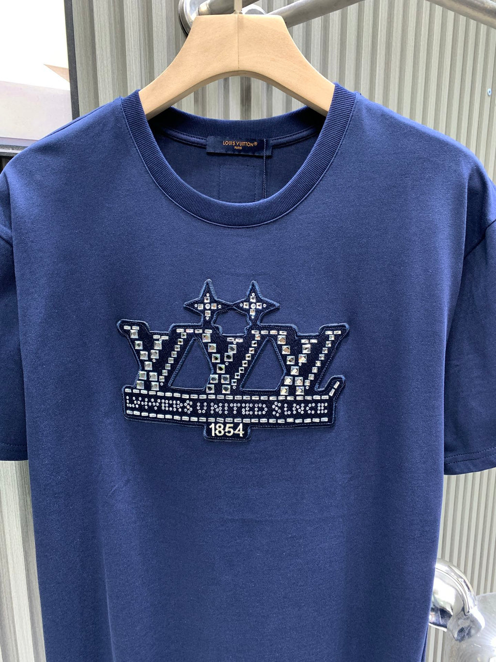 Blue T-shirt front with crown graphic and crew neckline on hanger.