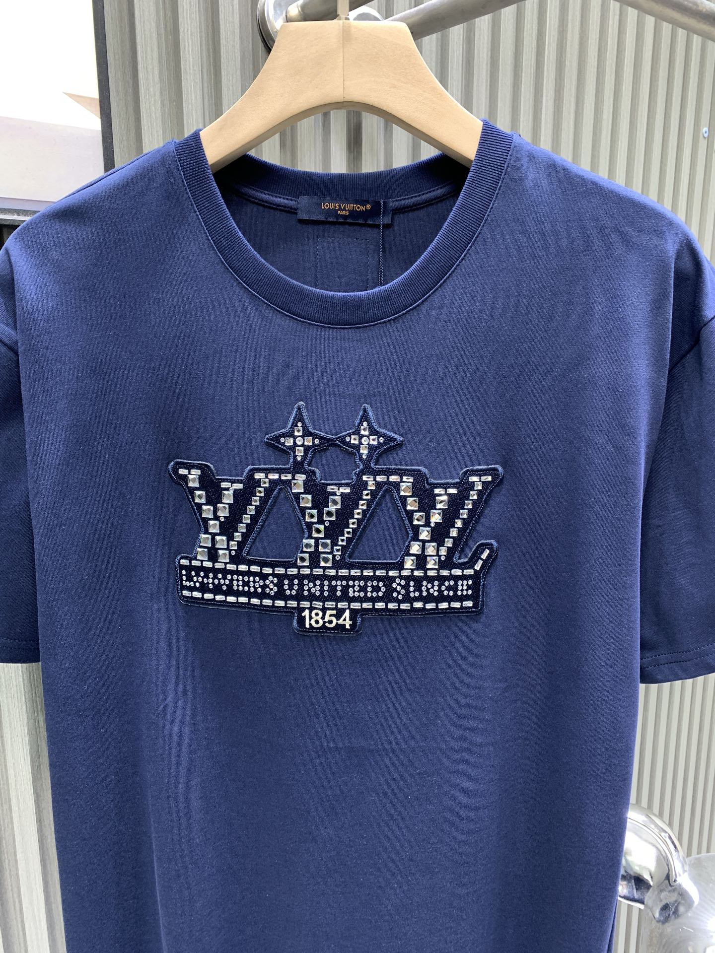 Blue T-shirt front with crown graphic and crew neckline on hanger.