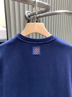 Blue T-shirt back view with small logo patch near the neckline.