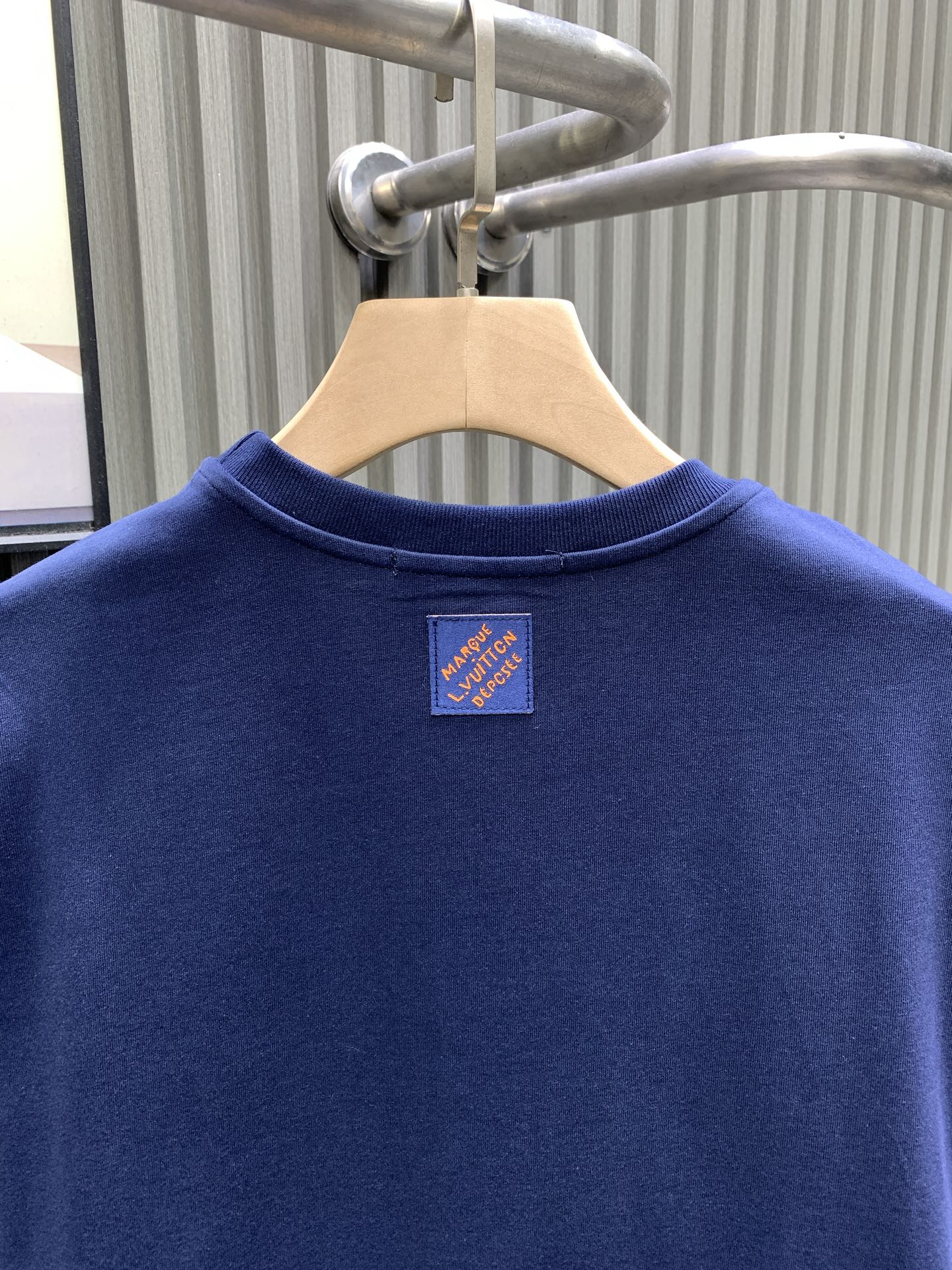 Blue T-shirt back view with small logo patch near the neckline.