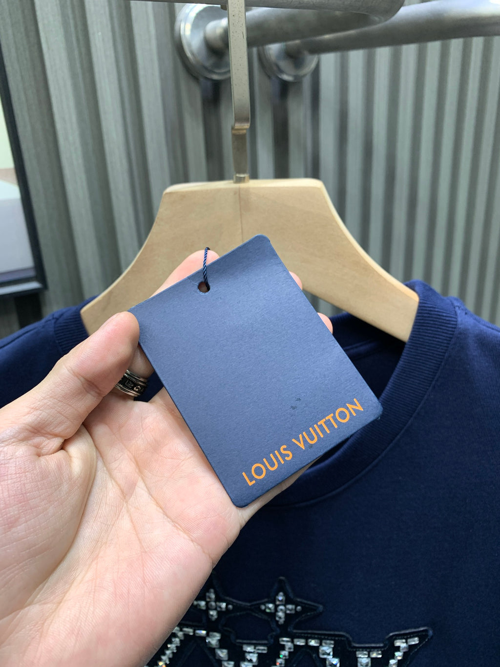 Blue T-shirt with brand tag label held near the neckline; crown graphic visible.