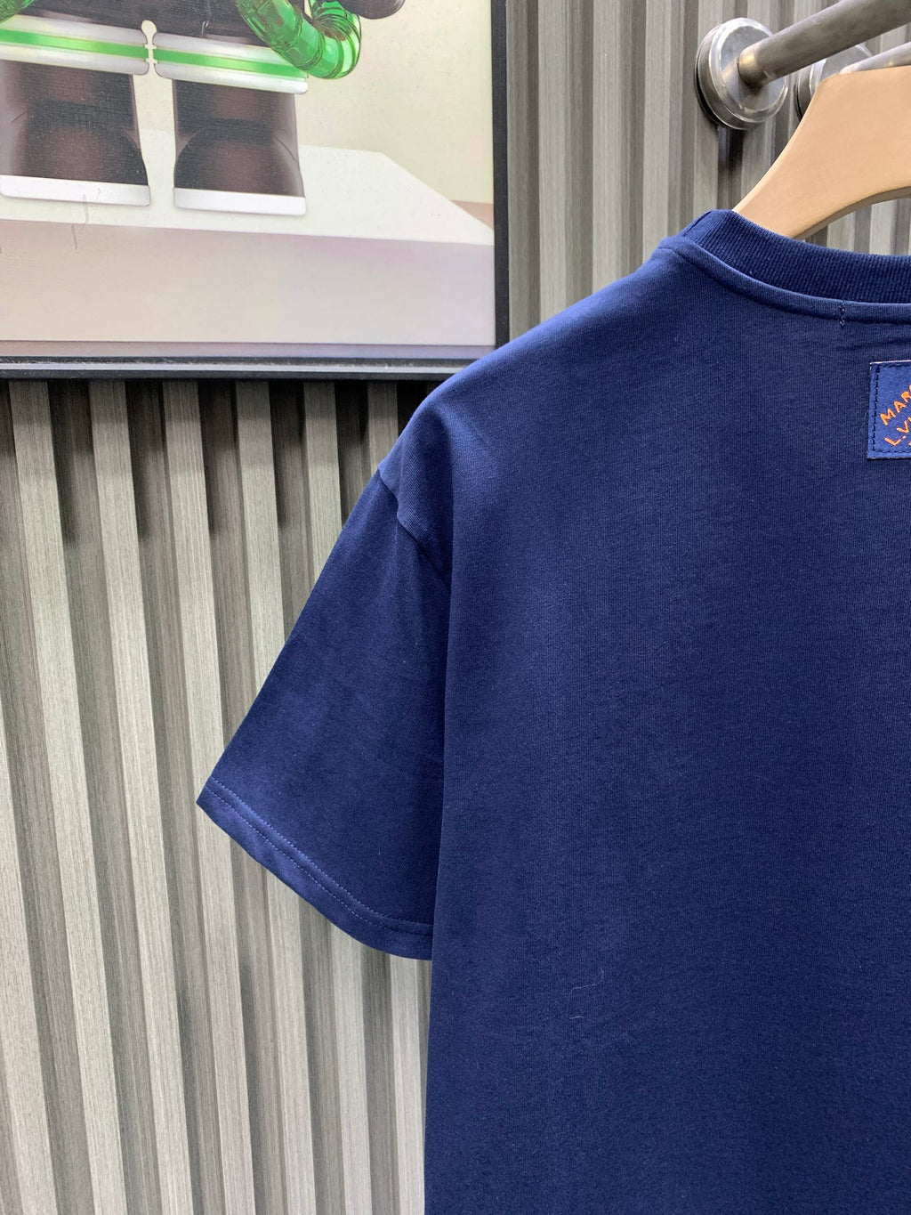 Blue T-shirt back partial view with small neck logo patch.