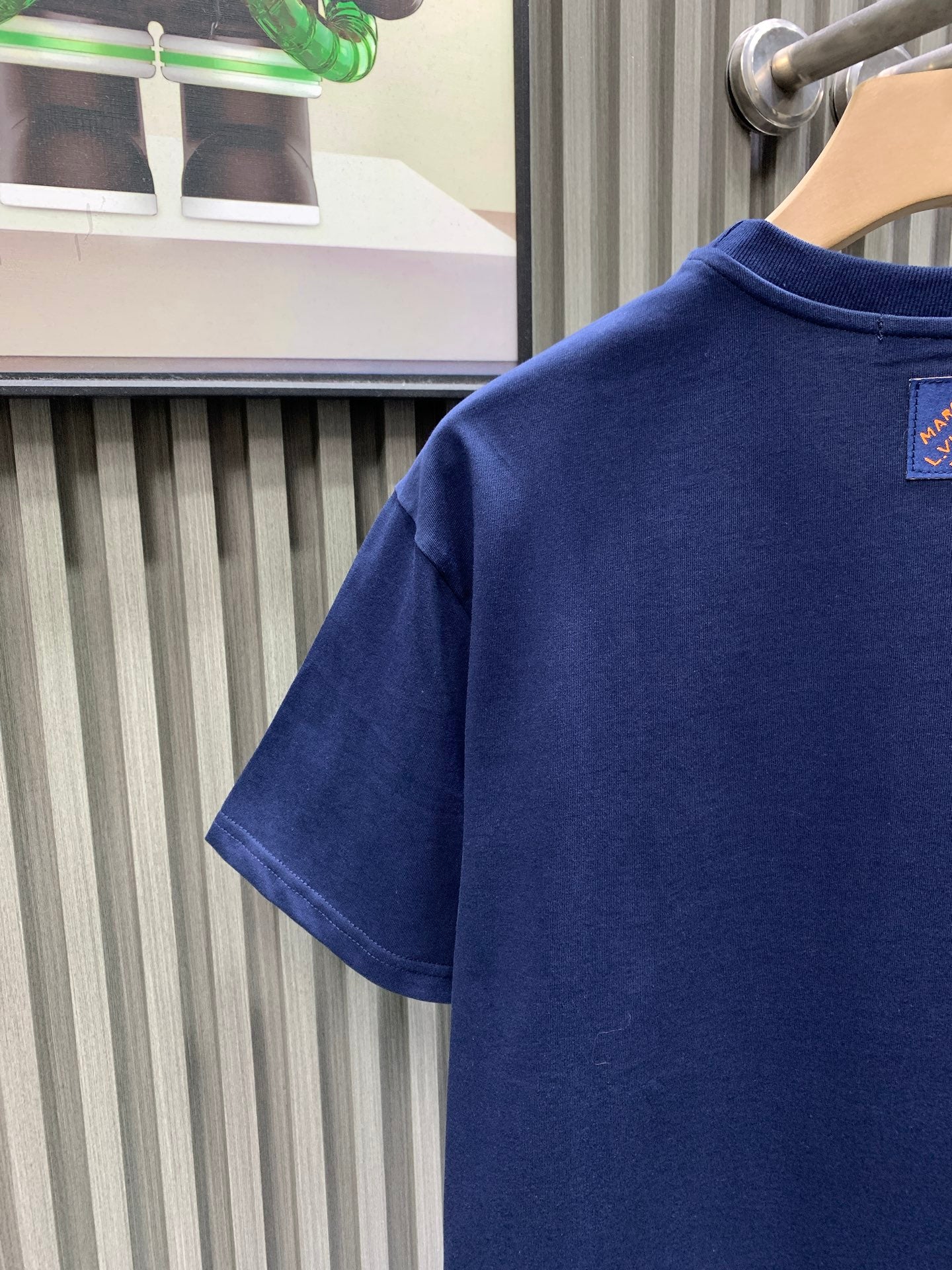 Blue T-shirt back partial view with small neck logo patch.