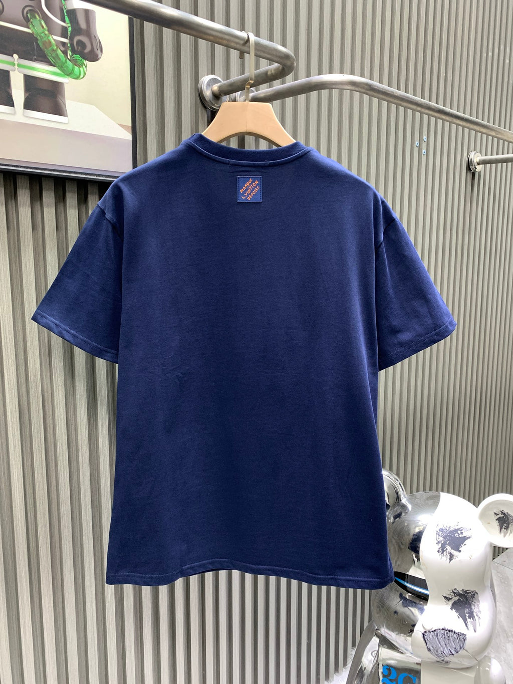 Blue T-shirt back view with small neck logo patch at center.