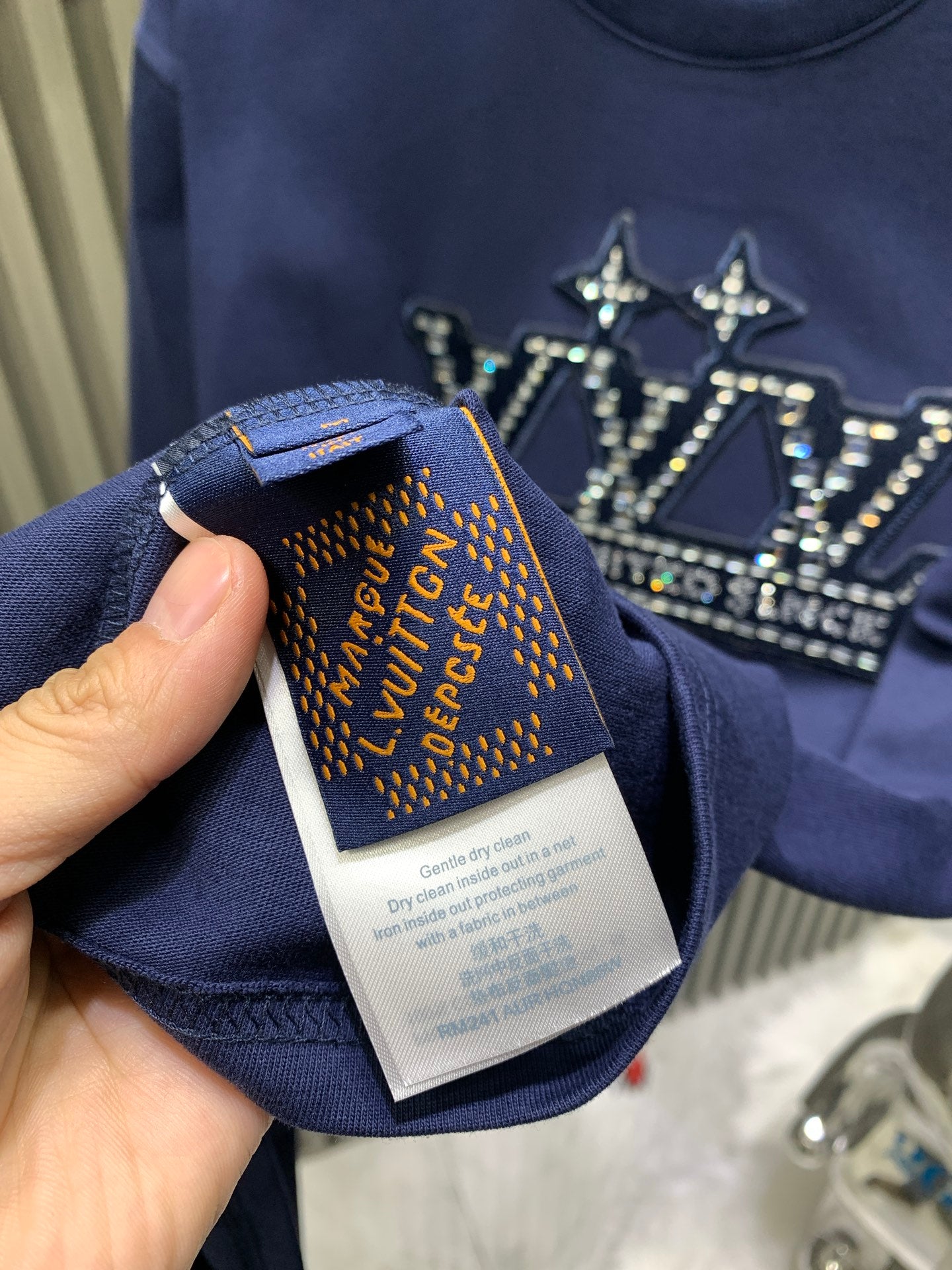 Blue T-shirt fabric care label and neckline tag held by hand.