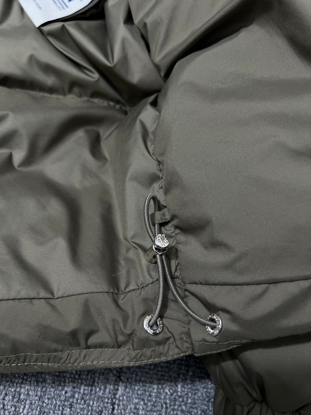Puffer jacket hem with drawstring and small logo patch on olive lining