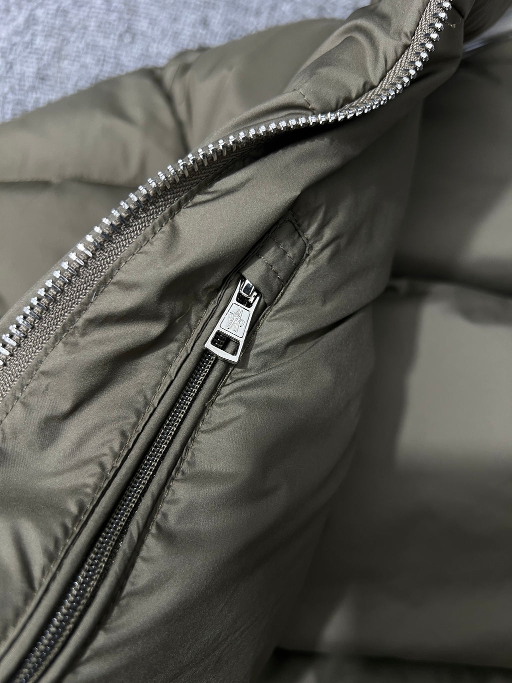 Puffer jacket close-up of metal zipper pull and olive fabric with snap tag