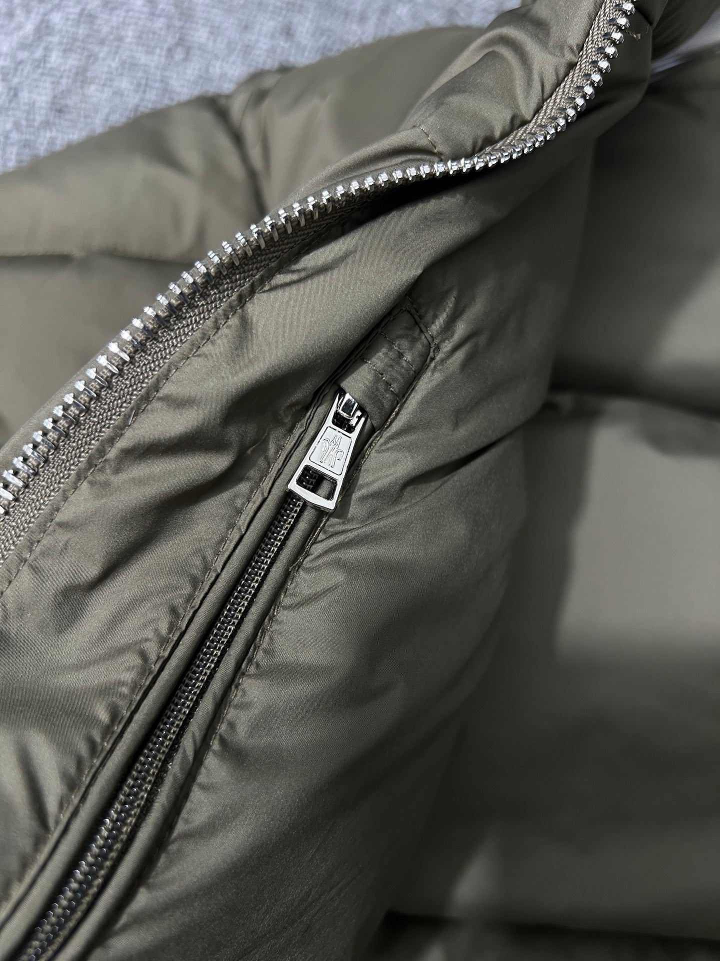 Puffer jacket close-up of metal zipper pull and olive fabric with snap tag