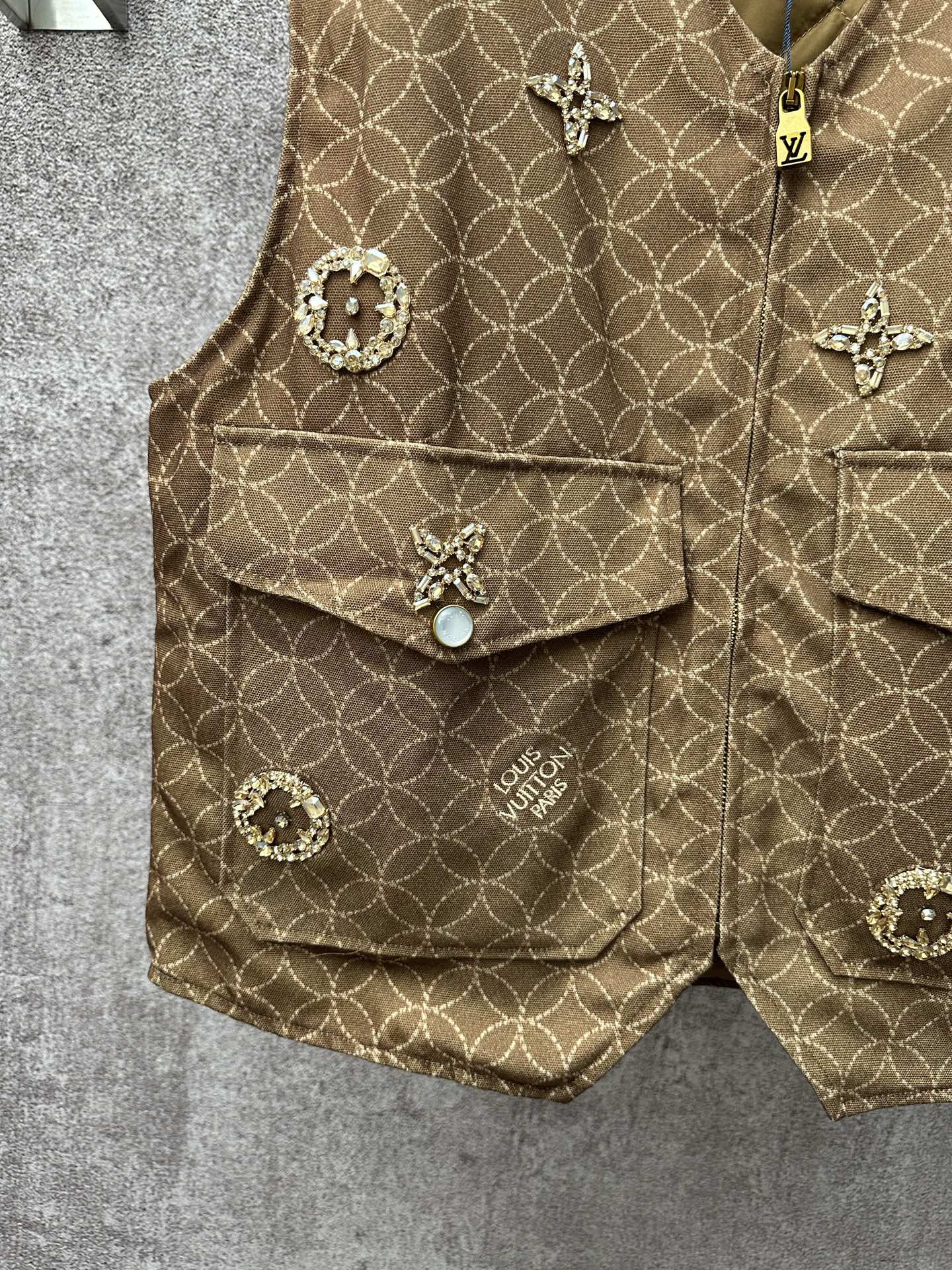 Gold monogram sleeveless vest with flap pockets and round decorative buttons, close-up