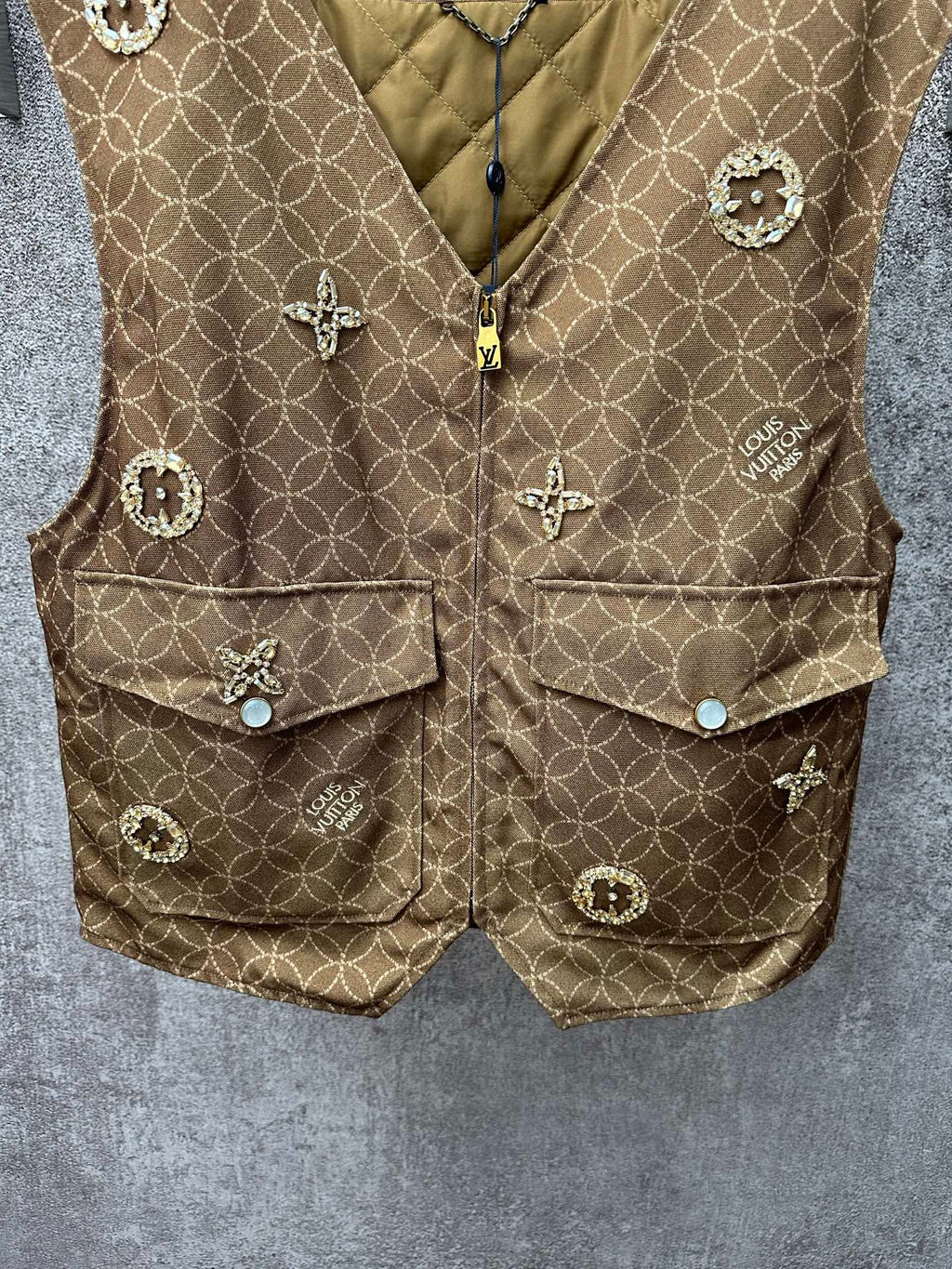 Gold monogram sleeveless vest with zip front, flap pockets, and small decorative charms