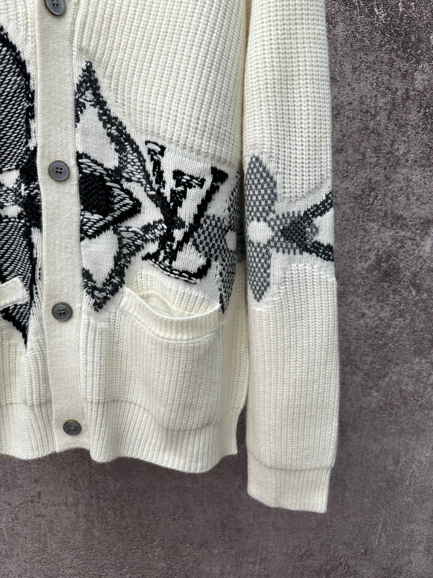 Cream cardigan sleeve and pocket detail with black butterfly-style motif embroidery