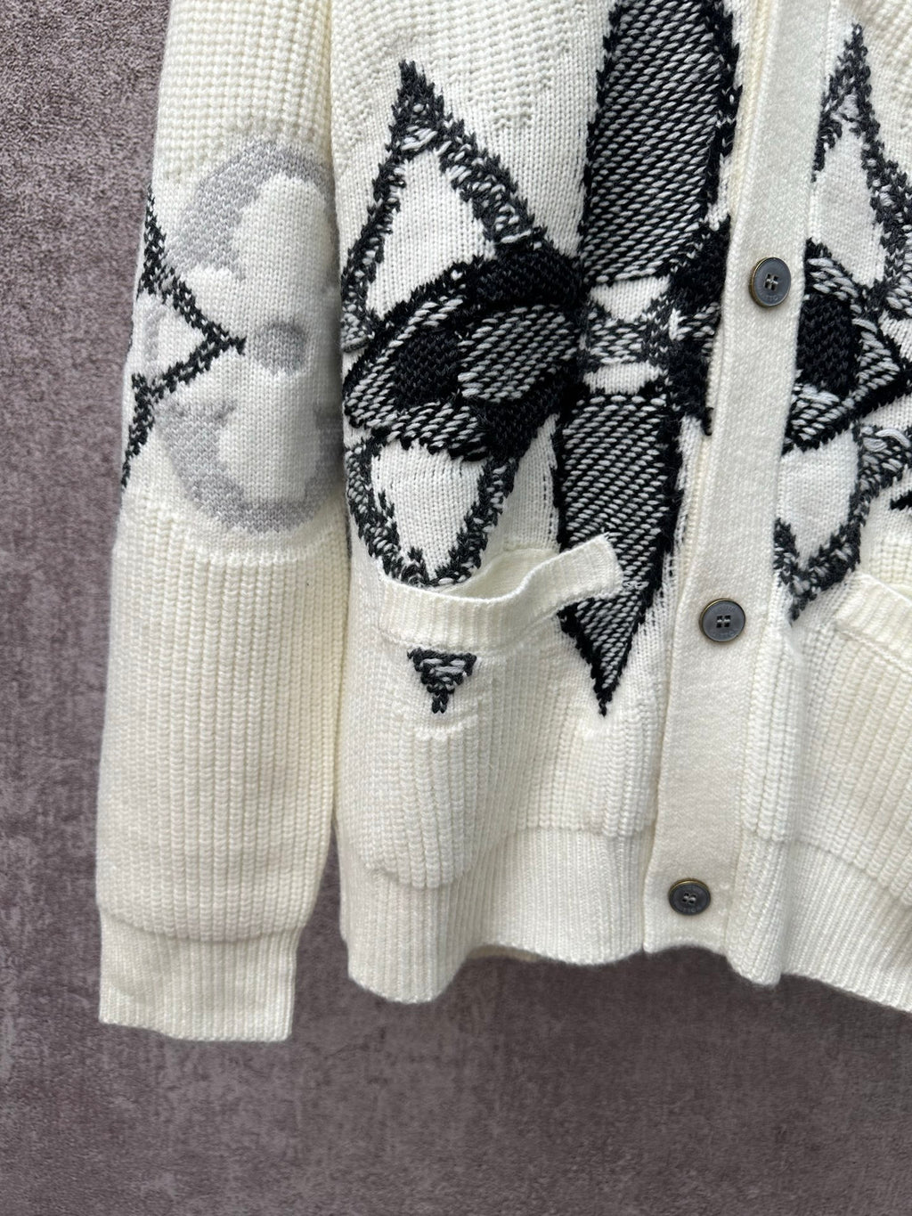 Cream cardigan with black butterfly-style embroidery over chest and patch pocket