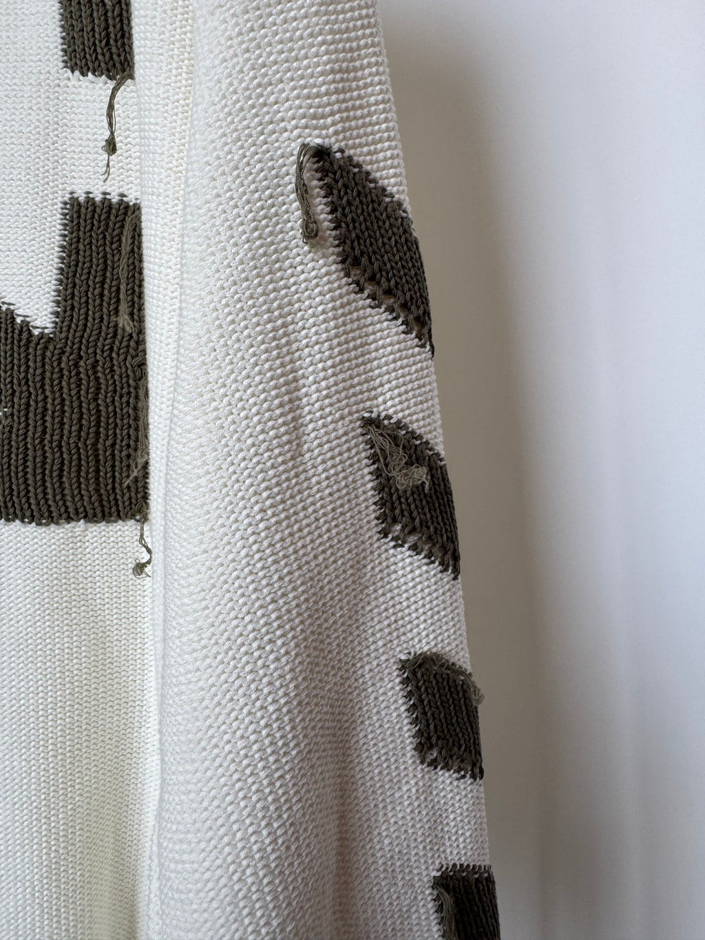 Off-white sweater sleeve with small black geometric knit patches